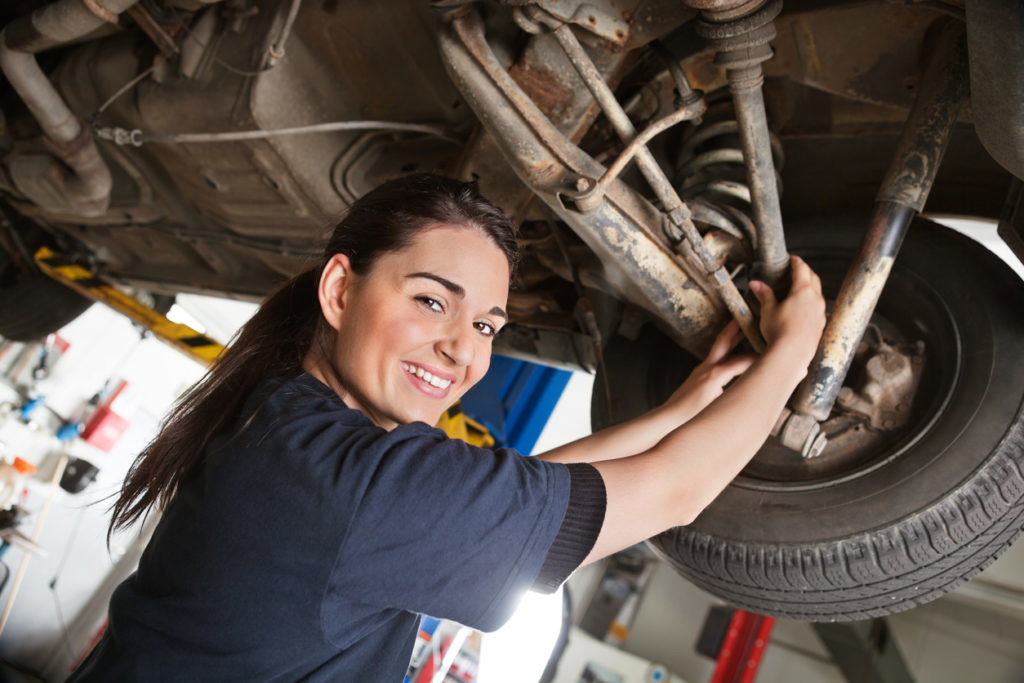 Portrait of smiling young female mechanic inspecting a CV joing on a car in auto repair shop