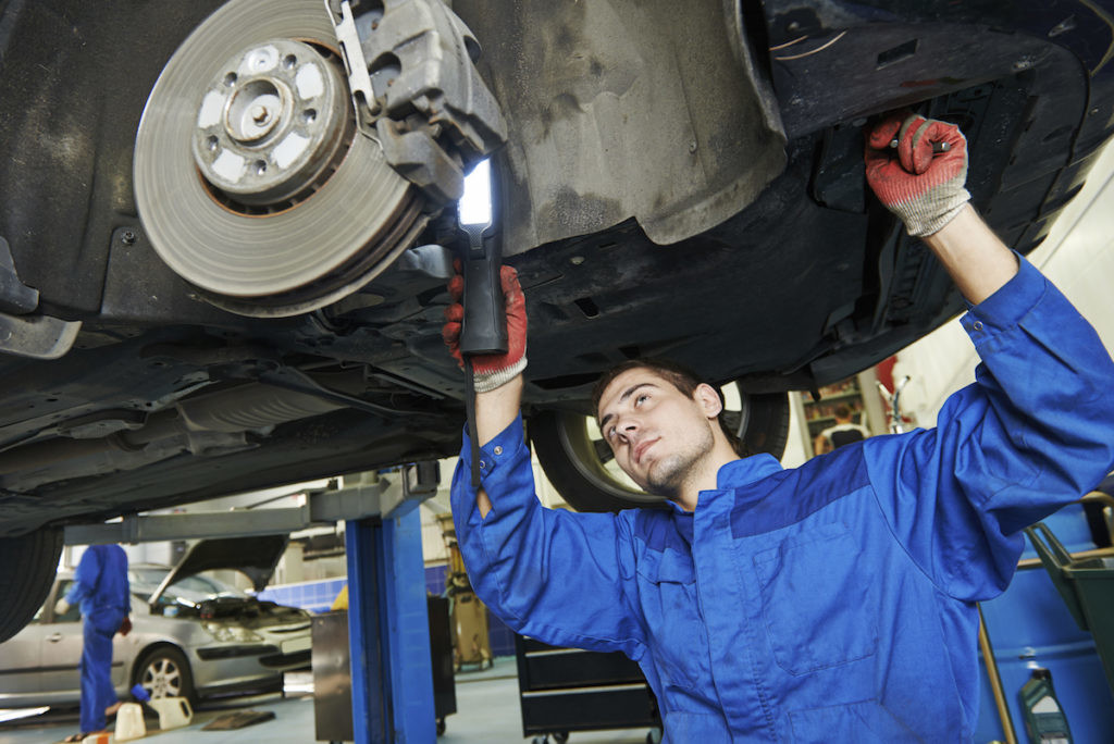 car mechanic examining car wheel brake disc and shoes of lifted automobile at repair service station
