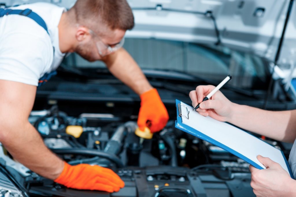 Running diagnostics. Two handsome car mechanics in uniform checking the engine under hood in the car service station and checking in service order