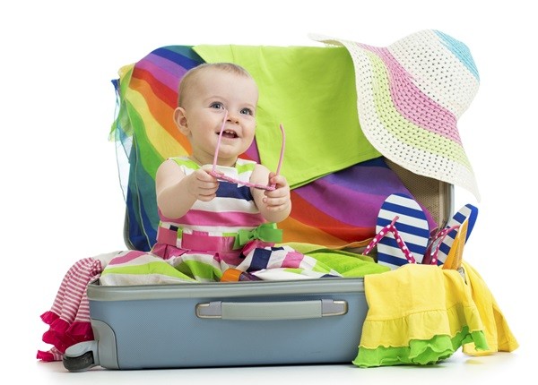 Baby girl sitting in suitcase with things for vacation travel
