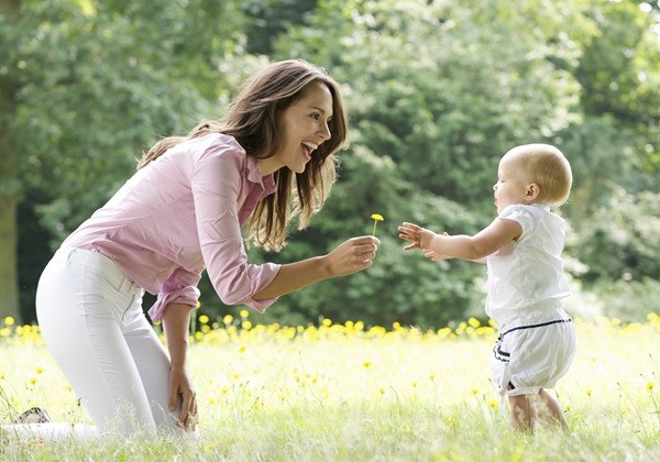 Portrait of a happy mother teaching baby to walk in the park