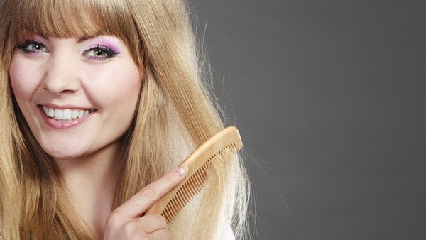 Fashion beauty and haircare concept. Closeup blonde woman refreshing her hairstyle girl combing hair with wooden comb gray background
